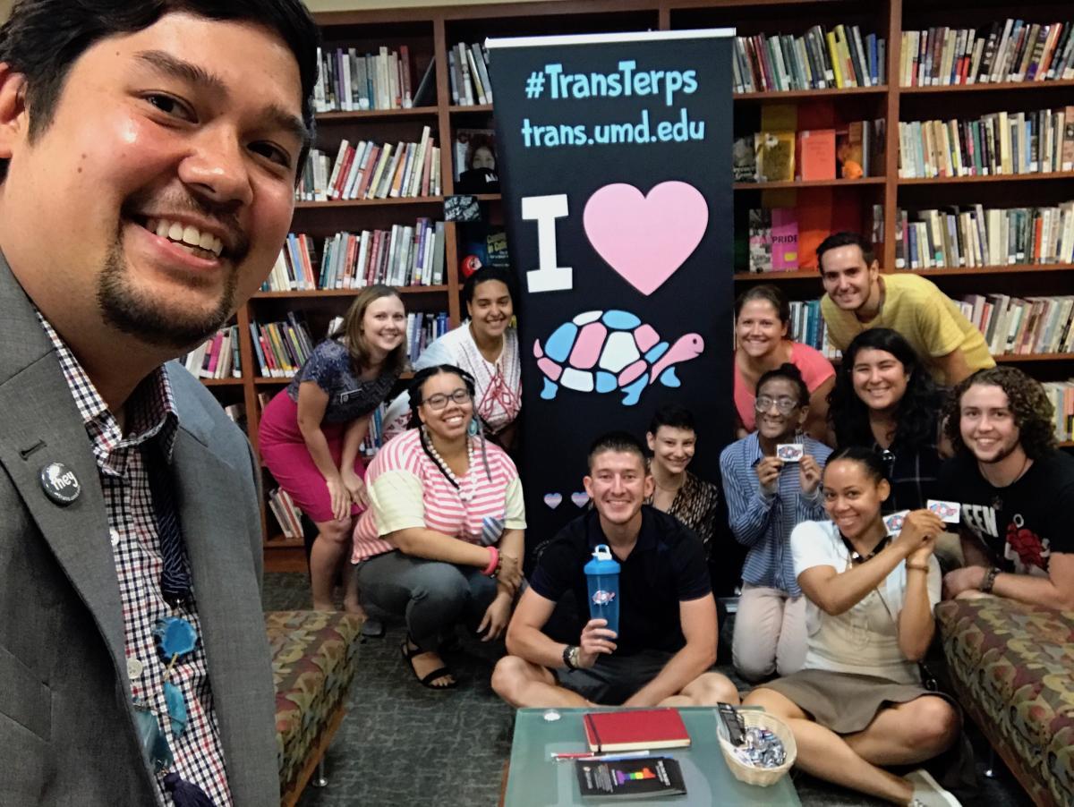 Smiling group selfie in front of a big Trans Terps sign
